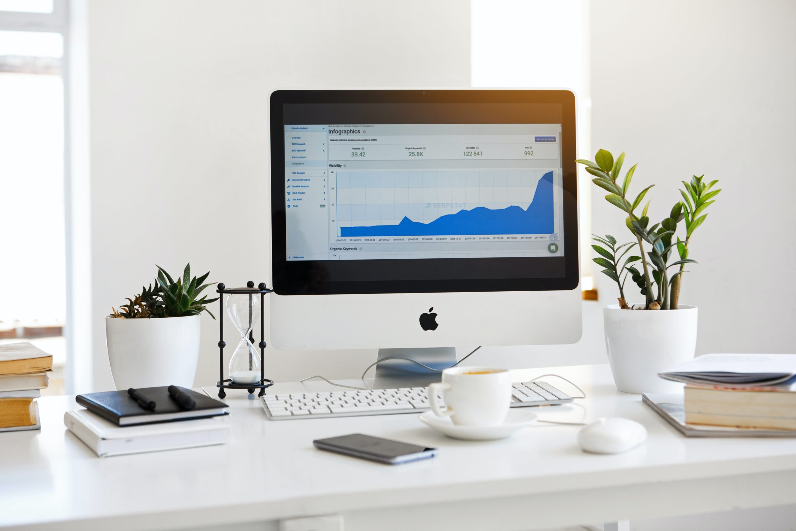 a Desktop Computer, an apple desktop computer with an iphone and cup of coffee on a white desk