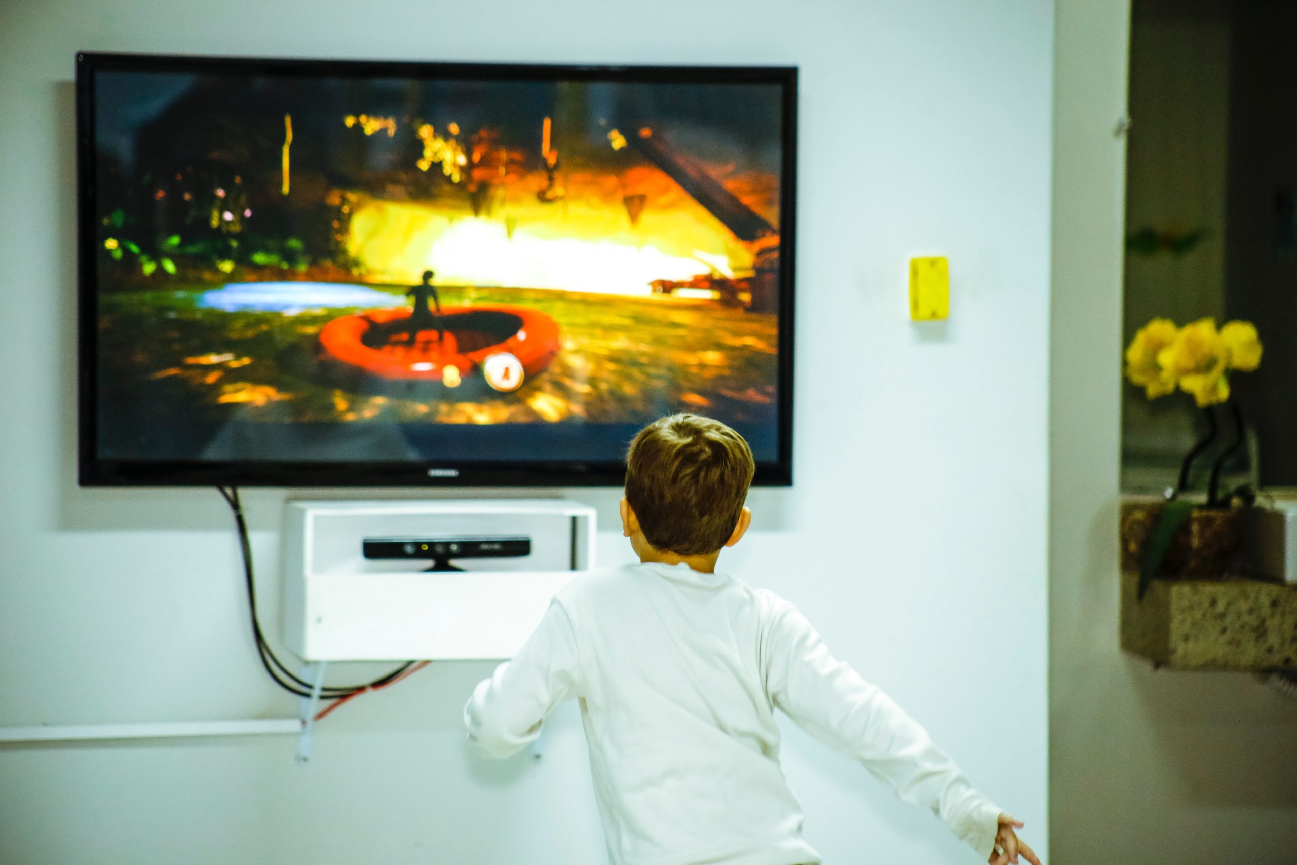 a boy in a white shirt is standing by a tv