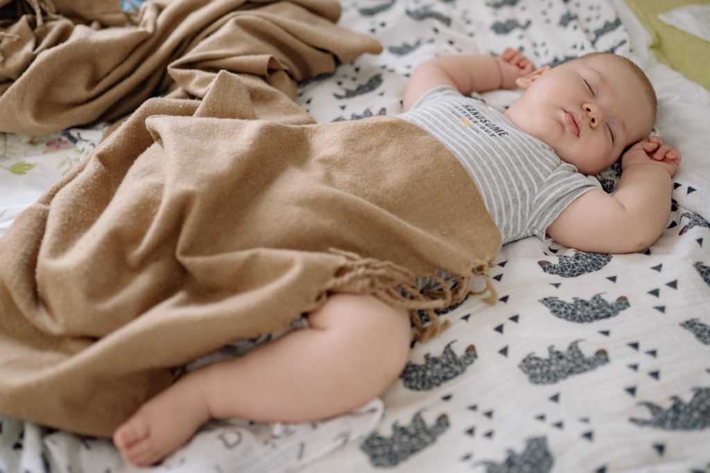 sleeping baby covered in a brown blanket, how to shop for a baby blanket