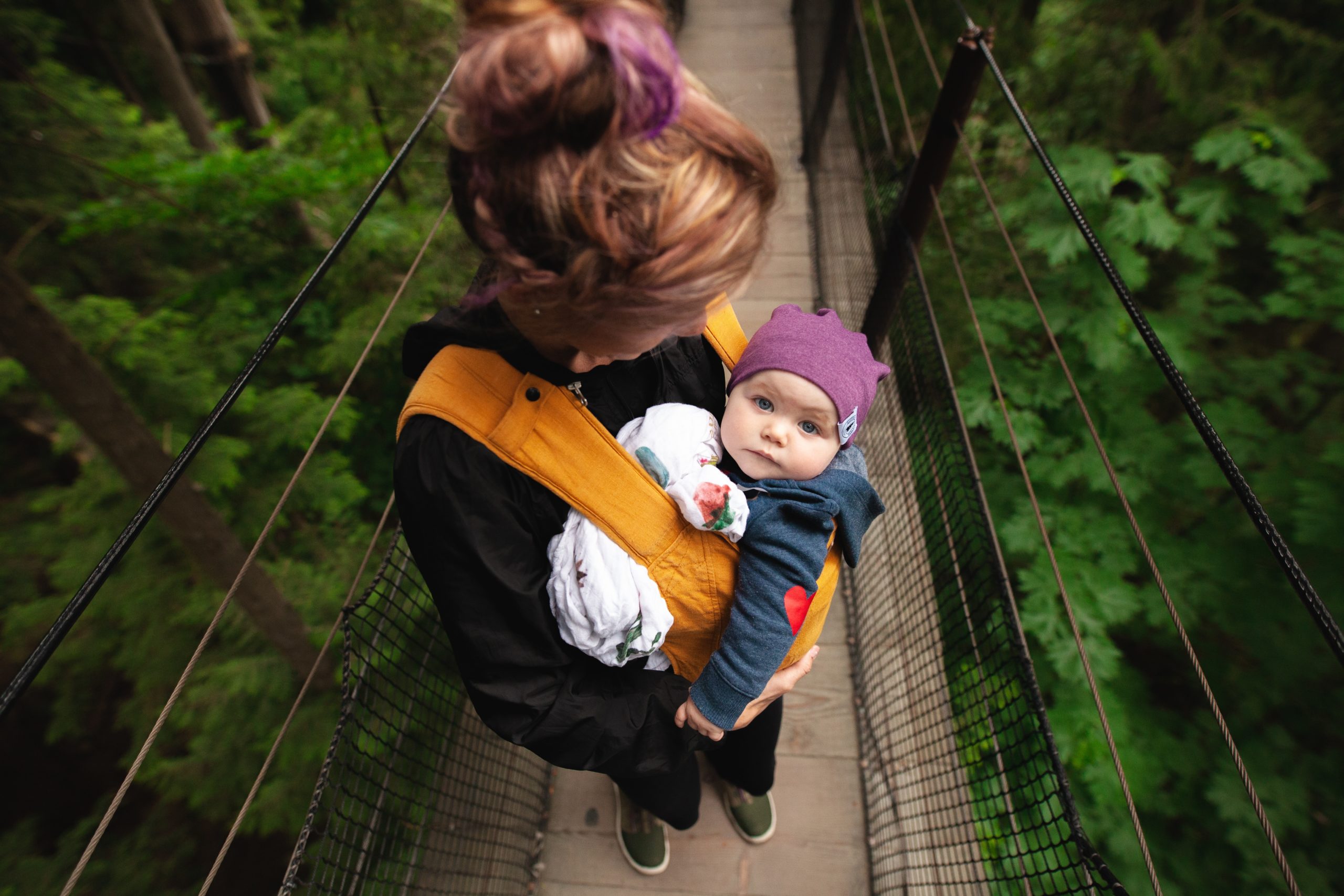 a woman is carrying her baby on a bridge with a baby carrier