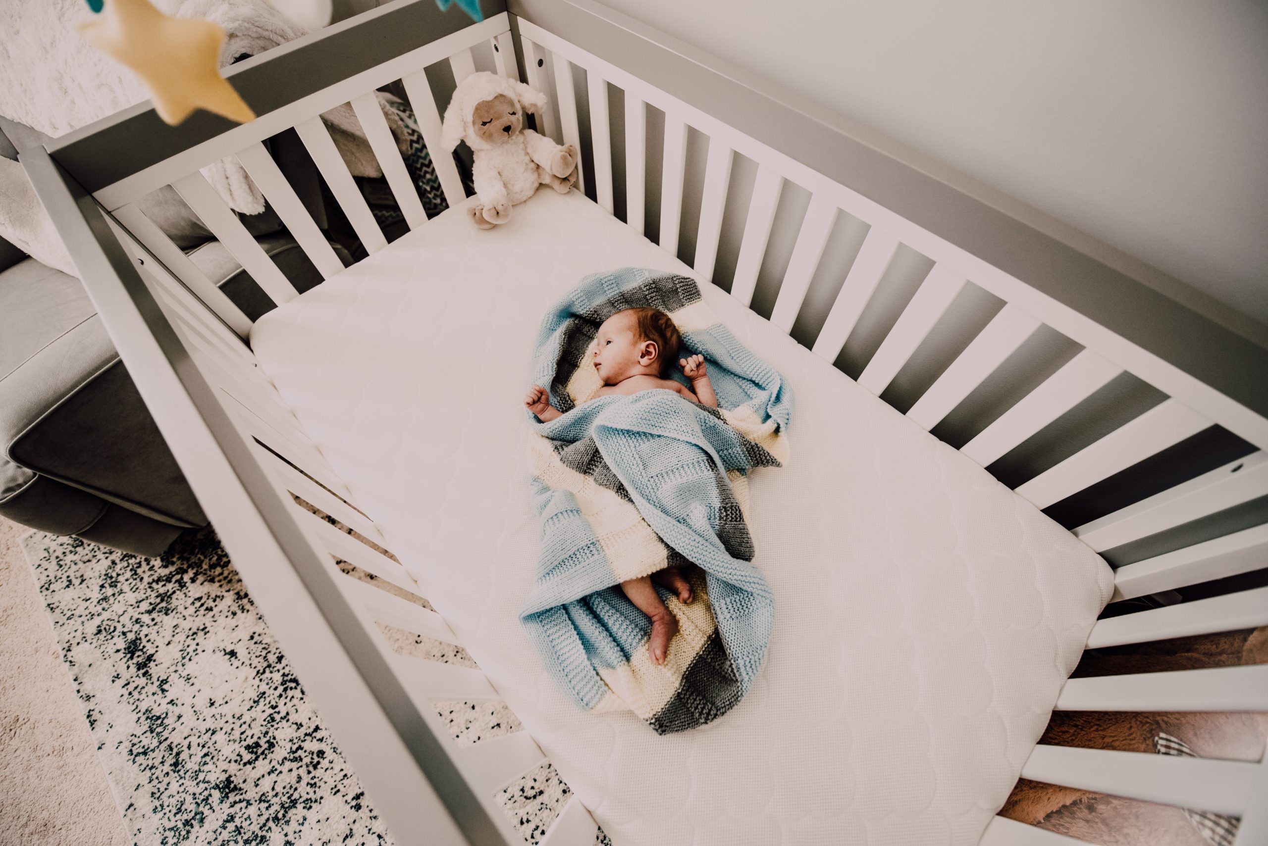 a baby covered in a blue blanket in a white crib